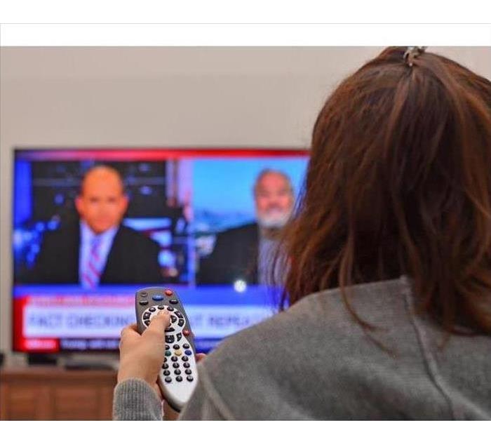 girl with control remote pointing at TV while watching news